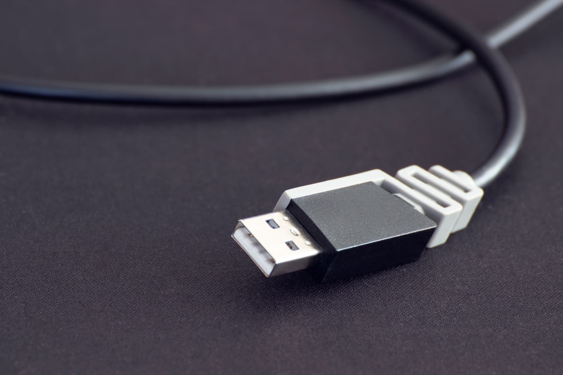 Close-up of a black USB plug and its cable on a dark surface.